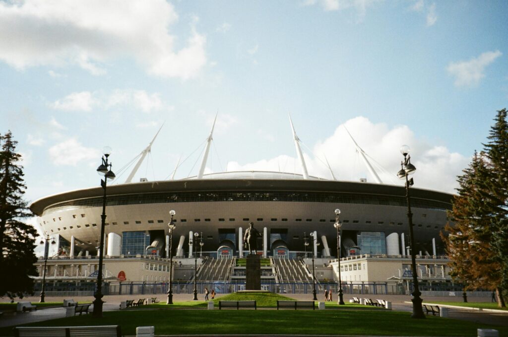 Front view of Gazprom Arena stadium in Saint Petersburg with clear skies and surrounding park area.